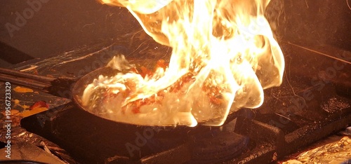flambering scene in akitchen, intense orange and yellow flames erupting from a frying pan 