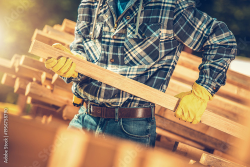 Worker Lifts Wooden Plank at Construction Site in Daylight