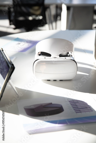 White VR headset resting centered on meeting table, left tablet and printed charts showing graphs