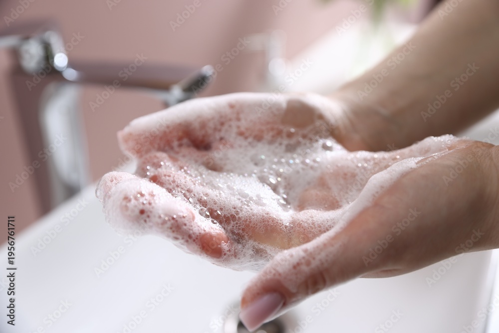 Fototapeta premium Woman washing hands with soap near white sink indoors, closeup