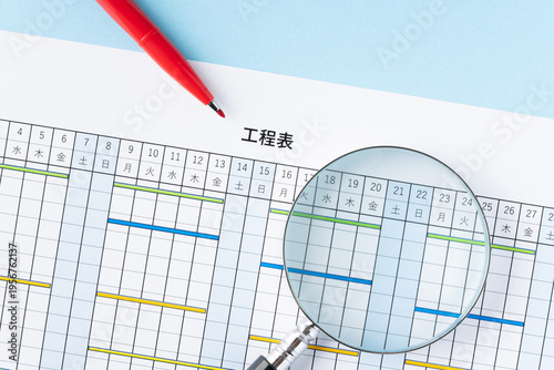 工程表と虫眼鏡と赤いペン