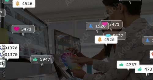 Designer using tablet color-wheel, peer pointing, badges overlapping monitors after sharing designs