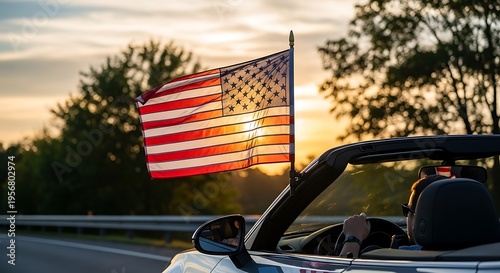 A person drives a convertible car with an american flag mounted during a beautiful golden sunset