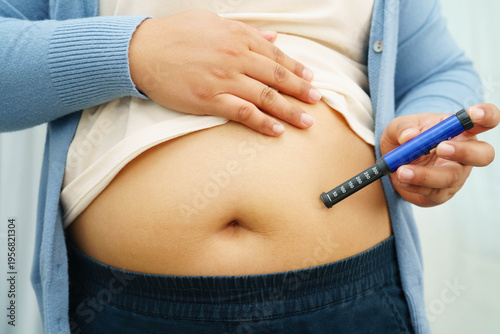 Asian woman injecting herself diabetes injecting insulin in stomach at home.