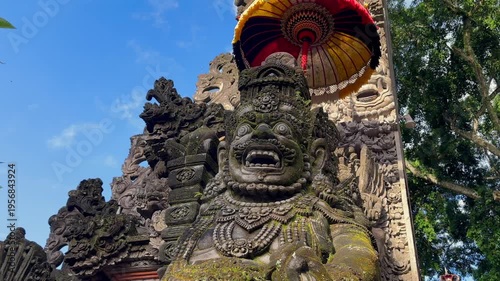 Traditional Balinese stone guardian statues at Hindu temple entrance in Bali, Indonesia. Sacred architecture with symbolic carvings and parasols. Concepts of religon, culture, and travel. 