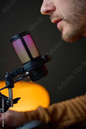 Side view of man speaking into studio microphone against dark background. Concept of podcasting audio recording and voiceover or livestream content