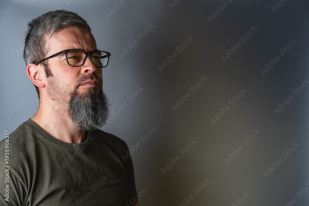 Fototapeta premium Man with glasses stands in profile with serious expression in studio