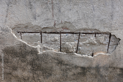 section of a damaged concrete wall revealing rusted iron reinforcement bars inside a large crack