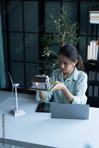 Engineer working on sustainable energy solar house model and wind turbine with laptop
