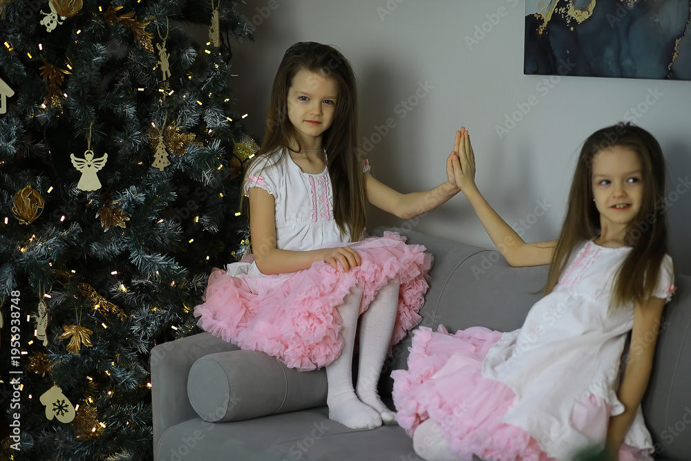 Obraz premium Twin Girls in Pink Dresses Sitting by Christmas Tree, Celebrating Holiday Season