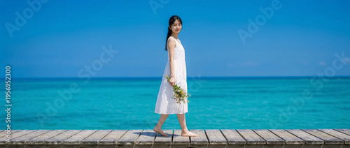 Authentic Asian woman holds flowers walking on a wooden pier near turquoise sea water