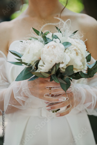 The bride holds a bouquet in her hands. The bride's hands are in gloves