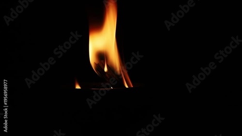 Close up of a bright fire flame burning on a wooden torch or bonfire in pitch black darkness. Concept of light, survival, heat, and energy. Abstract element of wild fire, danger.