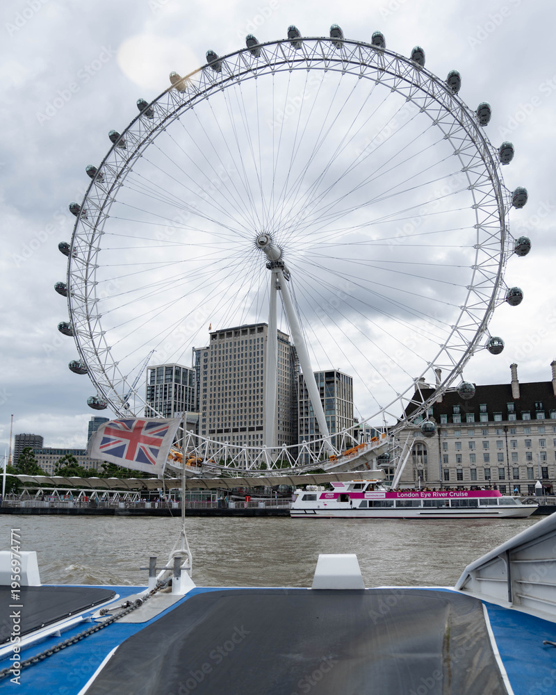 Fototapeta premium London, United Kingdom, 13 July 2023, The London Wheel rises above the Thames in central London. A river vessel passes below the wheel during daytime.