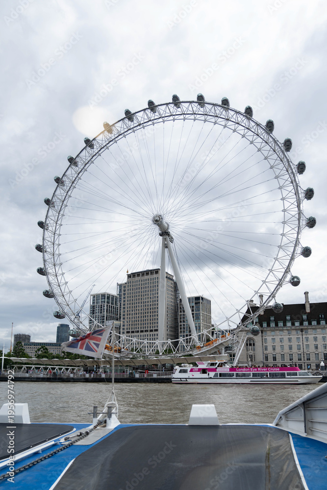 Fototapeta premium London, United Kingdom, 13 July 2023, The London Wheel rises above the Thames in central London. A river vessel passes below the wheel during daytime.