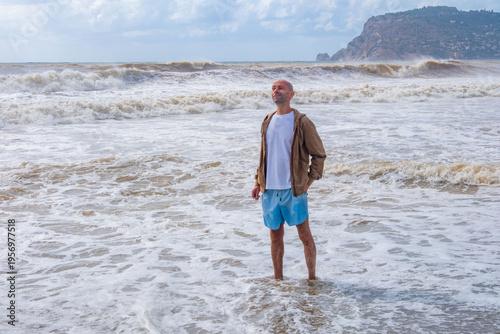 Foto happy positive caucasian Bald mature man walks barefoot in foamy surf, rough wav