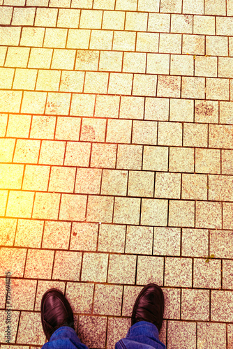 Person standing on a paved pathway with gray stones during daylight in an urban area