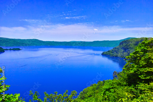 新緑の青森県十和田市にある十和田湖、湖面を行く観光船と新緑の景観
