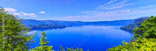 新緑の青森県十和田市にある十和田湖のパノラマ、湖面を行く観光船と新緑の景観

