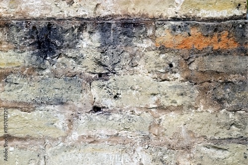 Weathered brick wall showcasing varied textures and colors, including beige, orange, and black, revealing its aged character.