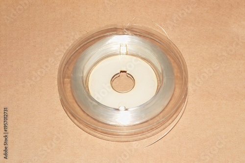 Vintage fishing spool with thin clear fishing line, coiled around plastic core, resting on brown surface with light reflections, glossy texture.