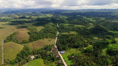 Aerial view of a winding road passing through the unique Chocolate Hills of Bohol, Philippines. Capturing the rural island infrastructure amidst a world-famous natural wonder