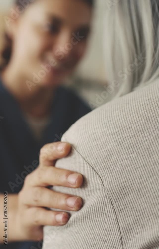 Healthcare worker touching elderly patient's shoulder with compassion and talking
