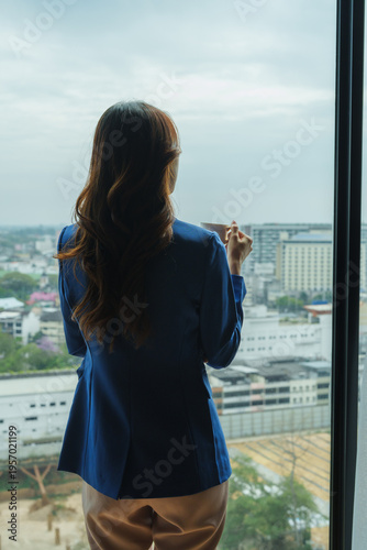 Woman holding cup looking out city window