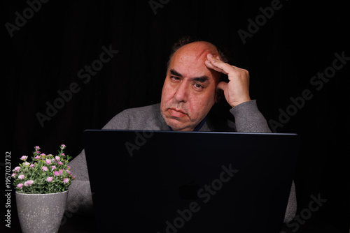 Принти на полотні Perplexed senior citizen holding a credit card and looking at a laptop computer while feeling defeated by a web checkout process