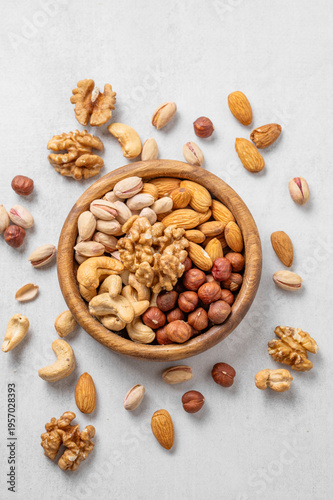 A mix of almonds, cashews, hazelnuts, walnuts, and pistachios in a wooden bowl on a light background.
