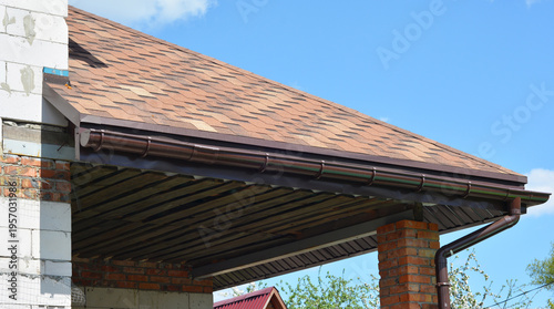 Asphalt shingle house roof with gutter installation.