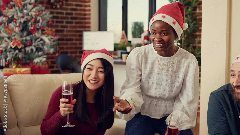 Obraz premium Multiethnic group of people clinking wine glasses at office party event, sitting on couch and making toast with alcohol to celebrate christmas eve. Being festive with alcoholic drink on xmas day.