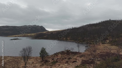 Aerial drone footage showing a mountain lake under cloudy weather conditions. The scene features calm water, surrounding mountainous terrain, and overcast skies, presenting a natural landscape with di