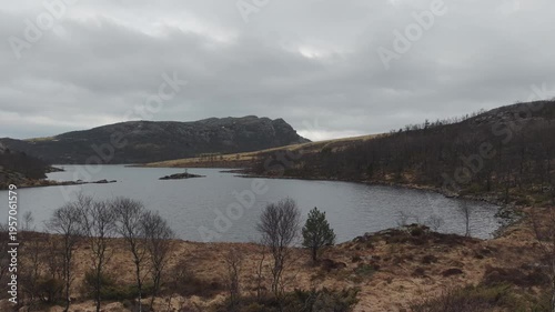 Aerial drone footage showing a mountain lake under cloudy weather conditions. The scene features calm water, surrounding mountainous terrain, and overcast skies, presenting a natural landscape with di