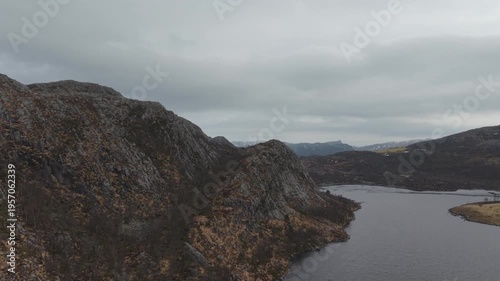 Aerial drone footage showing a mountain lake under cloudy weather conditions. The scene features calm water, surrounding mountainous terrain, and overcast skies, presenting a natural landscape with di