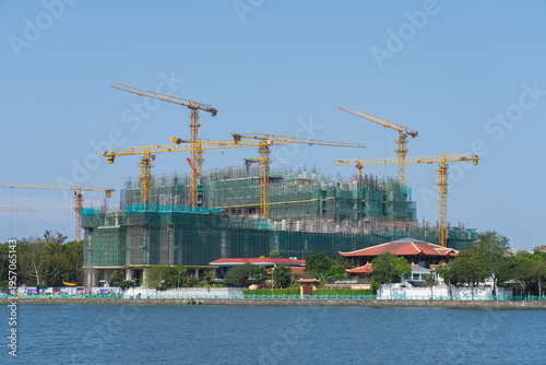 Construction cranes rise above a large building project near West Lake in Hanoi, showing rapid urban development beside the calm water.