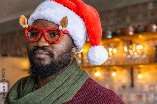 African American man in 30s wearing Santa-style hat, reindeer glasses and green scarf at cozy bar