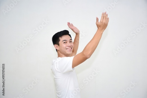 Young man with joyful expression raising hands and dancing against white background, showcasing happiness and energy in a carefree moment