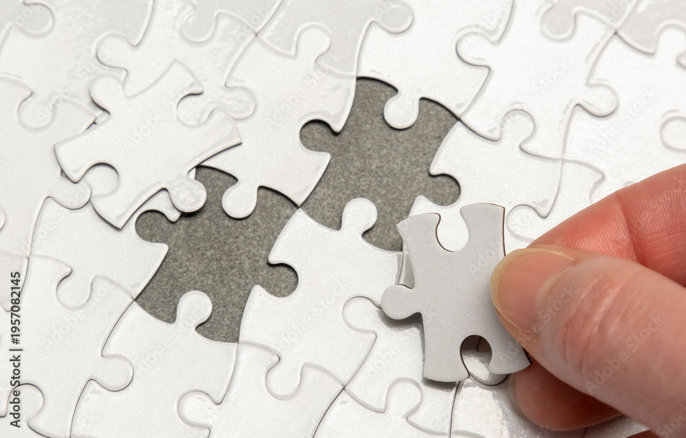 Fototapeta premium Puzzle pieces being arranged with one piece being placed in an empty spot on a grey surface