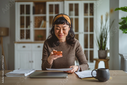 Obraz na płótnie Asian woman managing personal finances with smart phone at home