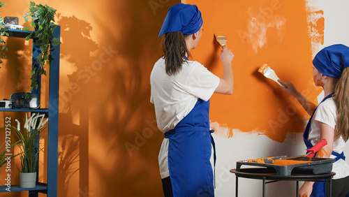 Fotografija Mother and kid using orange paint to change walls color and do housework renovation with diy tools