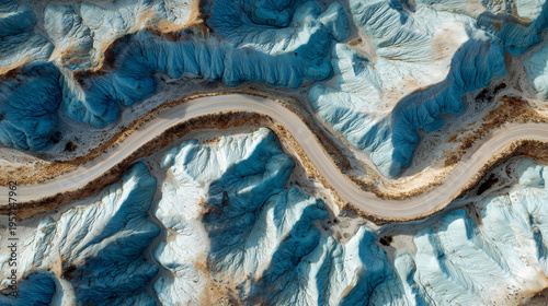 Aerial view of a winding road through a colorful, eroded desert landscape with blue and white clay formations.
