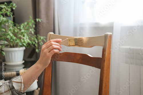 Fotografija Close-up of hand using a brush to apply beige paint to vintage wooden chair