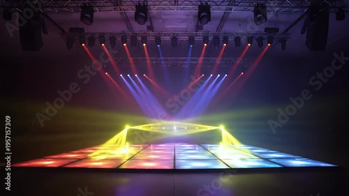 Stage lighting casts beams of red, yellow, and purple light onto a dark surface