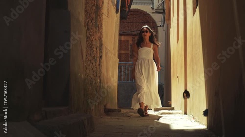 Woman tourist in white dress walks through beautiful Stone Town alley. Historic Zanzibar architecture and peaceful morning travel sightseeing.Popular travel destination Africa