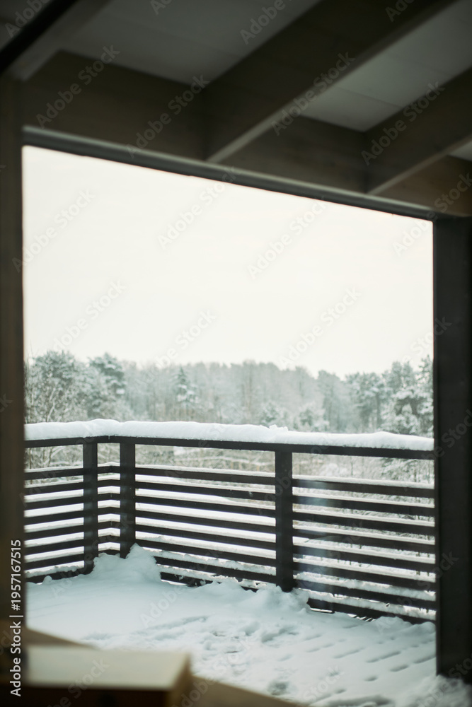 Fototapeta premium Snow covered balcony railing overlooking winter forest landscape with trees in background, outdoor scene showing untouched snow accumulation on wooden structure and ground, vertical