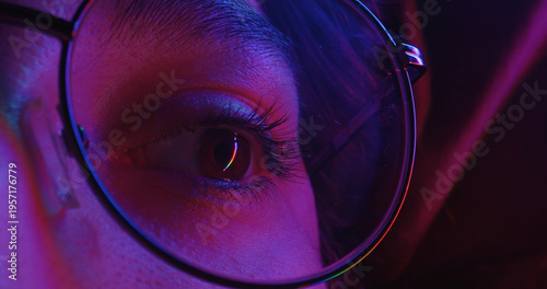 Fotografie A close up of eye framed by glasses illuminated by purple neon lights
