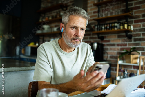 Middle-aged man checking smartphone while working from home kitchen