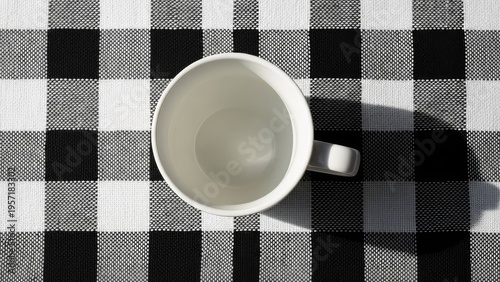 An empty white coffee mug on a black and white checkered tablecloth