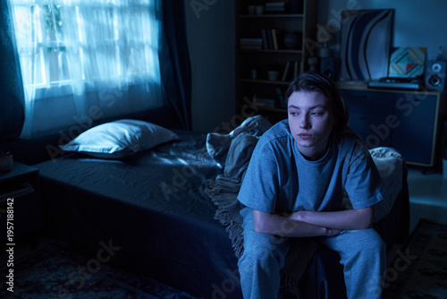 Bild auf Leinwand Young woman sitting on bed in dimly lit bedroom resting arms on knees looking aw